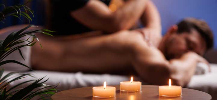 gay massage A person gets a back massage in a dim room with three candles on the table. male masseur
